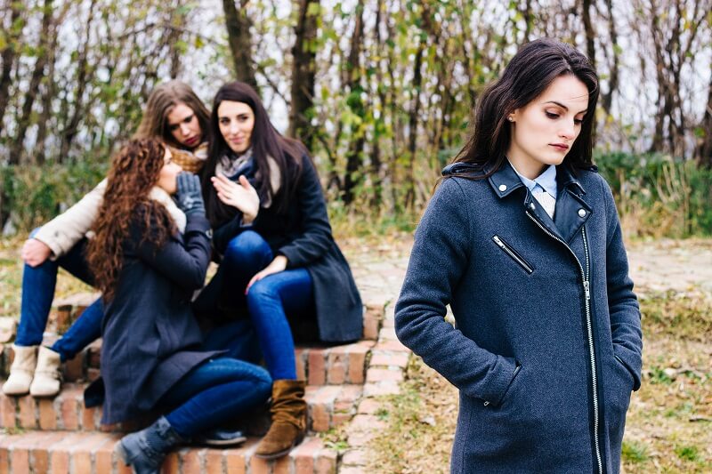 young girl walking away sad from another group of girls gossipping